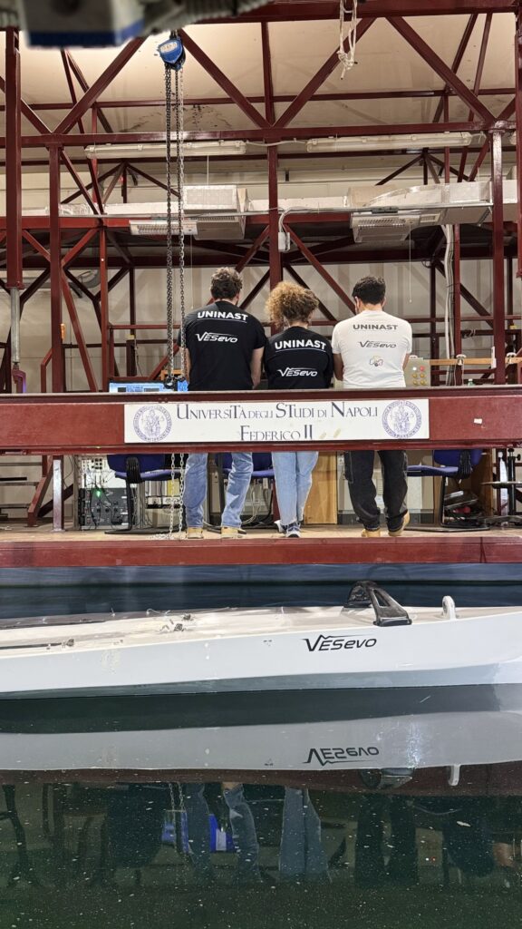 VESevo Smart Technologies, an innovative spin-off company of the University of Naples Federico II, announces a collaboration with UNINA Sailing Team, a leading team competing in the 1001Vela Cup. The regatta brings together Europe’s top universities in a competition that sees students testing the performance of sailboats they have engineered, designed and built
The team, also from the University of Naples Federico II, is composed of more than 50 students who design and build sailboats using natural and recycled materials, applying new approaches to improve structural efficiency. The collaboration enables the use of VESevo technology to support material testing and the evaluation of components employed in the construction of the sailboat.
As attention on competitive sailing grows ahead of next year’s America’s Cup in Naples, the collaboration introduces VESevo technology into a field where technical analysis plays an increasingly central role. The same testing principles used in motorsport are now being extended to sailing, supporting data driven engineering decisions in an entirely new competitive environment.

Andrea Genovese, Chief Executive Officer (CEO) of VESevo:
“The collaboration with UNINA Sailing Team opens a new chapter for VESevo, applying VESevo technology to a context different from traditional racing environments. The study of materials and components for competitive sailing involves factors specific to marine conditions, creating new scenarios for experimentation and technical development. With the VESevo device on board, students will be able to translate academic theory into measurable, real-world data, gaining hands-on experience. Emerging from an academic background, VESevo remains strongly committed to supporting student projects and helping train the next generation of engineers”
Giulia Correra, UNINA Sailing Team President:
“Working with VESevo is a great opportunity to show how a melting pot of skills and knowledges is the key for a wide spectrum research and perpetuation of progress while the interconnection of university realities is the light for a in good health education system. We are very happy to be part of VESevo network and honored to know this company found in our project a reality worthy of support. We know what giving support to a team so far form what is the main VESevo pourpose means and we feel all the responsibility about being in this collaboration, a great opportunity for a young renewed team.“
